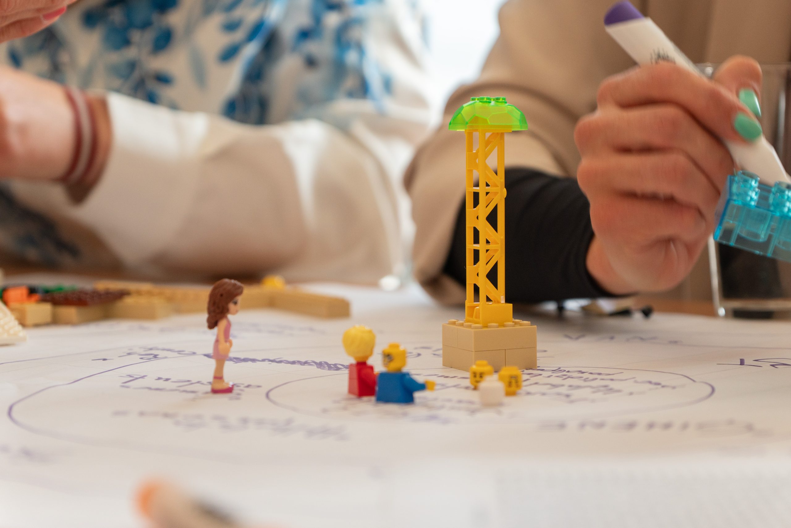Sociālie darbinieki darbnīcā veido simboliskas konstrukcijas no LEGO klučiem uz papīra ar ideju shēmām.