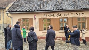 Cilvēki pie ēkas ar uzrakstu “Restaurācijas centrs” piedalās vizītē vai pasākumā