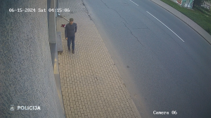 Videonovērošanas attēls, kurā redzams vīrietis, kas iet pa ietvi, bet uz zemes mētājas Latvijas karogs.