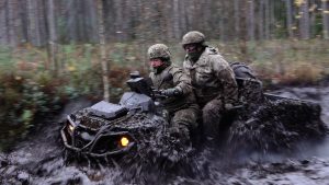 Divi karavīri ar sešriteņu visurgājēju brauc pa dubļainu meža ceļu militāro mācību laikā.