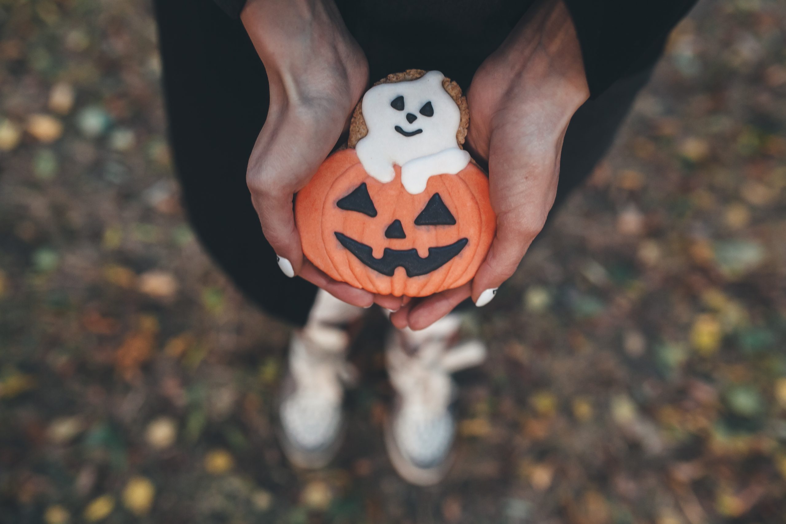 Rokas tur Helovīna tēmu cepumu – ķirbi ar izgrieztu seju un mazu spoku.