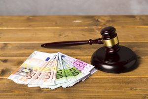 Tiesneša āmurs (gavels) un izklātas dažādu nominālu eiro banknotes uz koka galda.