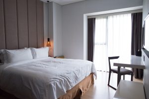 Moderni iekārtota viesnīcas istaba ar lielu gultu, galdu un logu ar aizkariem.