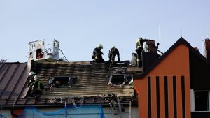 Ugunsdzēsēji dzēš ugunsgrēka sekas uz dzīvojamās mājas jumta