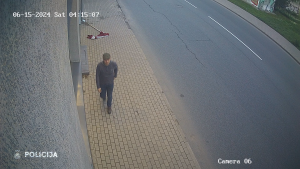 Videonovērošanas attēls, kurā redzams vīrietis, kas iet pa ietvi, bet uz zemes mētājas Latvijas karogs.