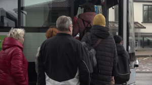 Cilvēki rindā iekāpj autobusā lietainā dienā.