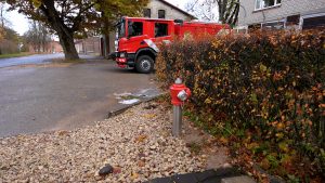 Ugunsdzēsēju automašīna pie depo, priekšplānā redzams ugunsdzēsības hidrants.