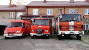 Trīs ugunsdzēsēju automašīnas stāv rindā pie depo ēkas.