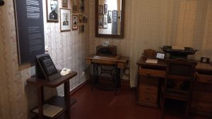 Vēsturiska istaba ar senām mēbelēm, fotogrāfiju galeriju un rakstāmmašīnu muzeja ekspozīcijā.