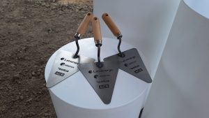 Trīs simboliskas celtniecības lāpstiņas ar uzņēmumu “Latvenergo”, “Elektrum”, “Eolus” un “ACB” logotipiem, novietotas uz balta postamenta būvobjekta teritorijā.