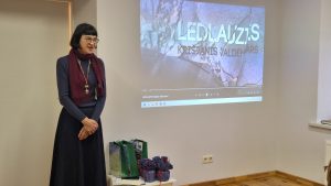 Sieviete stāv pie ekrāna, uz kura projicēts dokumentālās filmas kadrs par ledlauzi "Krišjānis Valdemārs"
