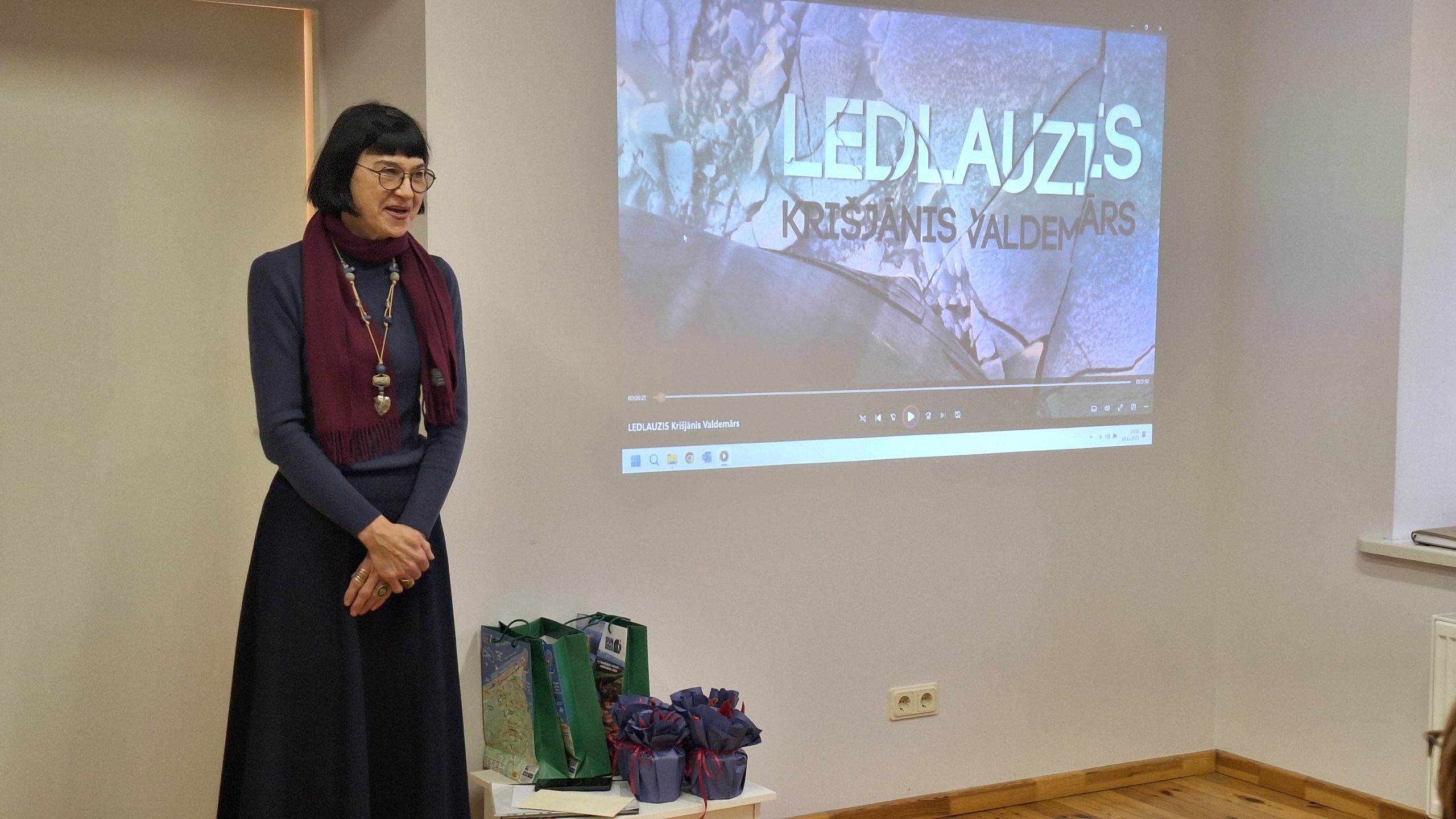 Sieviete stāv pie ekrāna, uz kura projicēts dokumentālās filmas kadrs par ledlauzi 