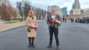 Rīgas mērs Viesturs Kleinbergs ar ziedu pušķi un BTA valdes locekle Evija Matveja ar apdrošināšanas maketu stāv pie Brīvības pieminekļa.