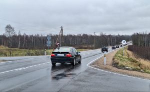 Mitrs lauku ceļš ar automašīnām un Latvijas karogu pie transporta.