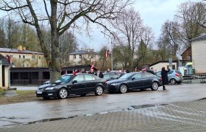 Cilvēki pie automašīnām ar Latvijas karogiem svētku pasākumā.