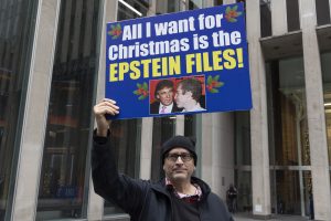 Demonstrants paceltā plakātā prasa publiskot "Epstein Files" (Epstīna lietas dokumentus). Uz plakāta redzama Donalda Trampa un Džefrija Epstīna bilde.