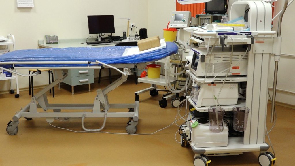 Medicīnas procedūru telpa ar pārvietojamu operāciju galdu un aprīkojumu.