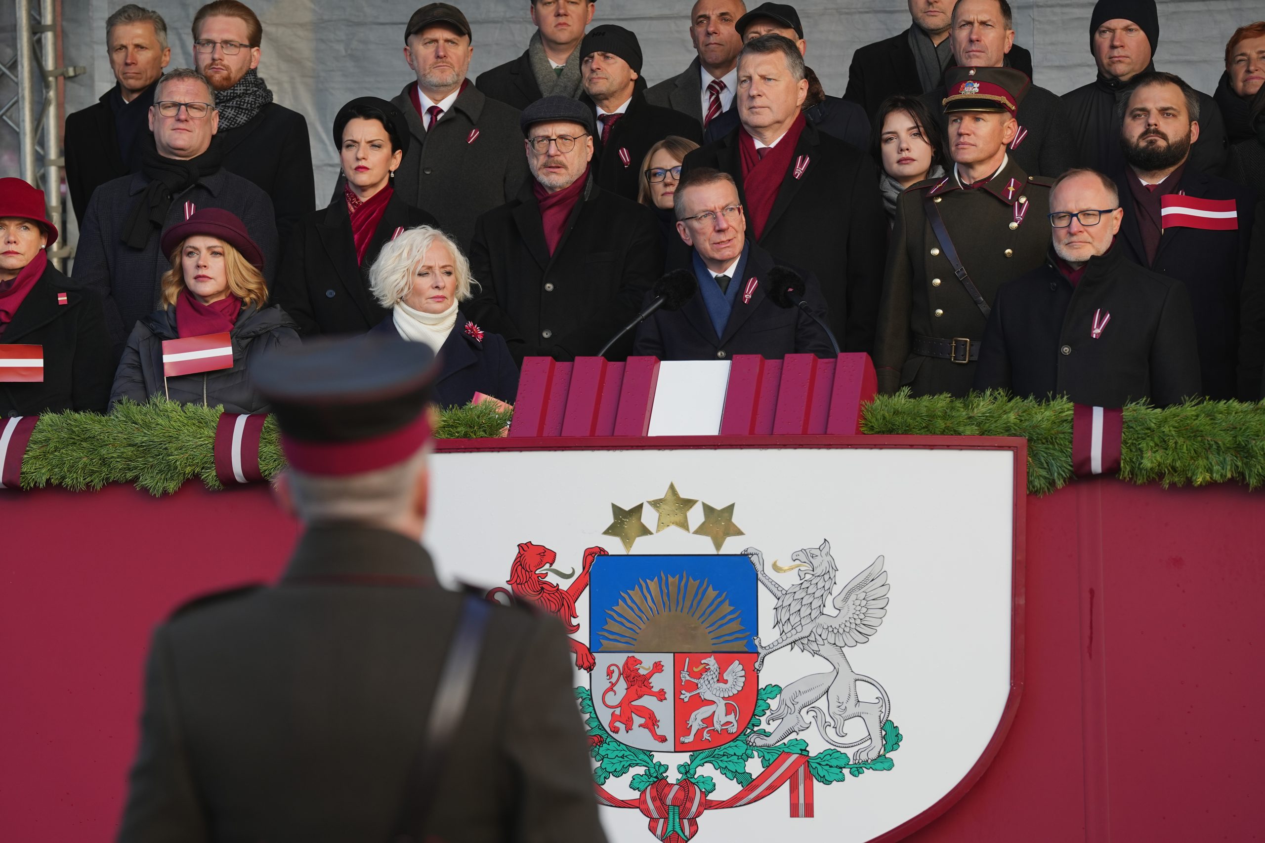 Cilvēki svinīgā pasākumā pie Latvijas ģerboņa tribīnes valsts svētku laikā.