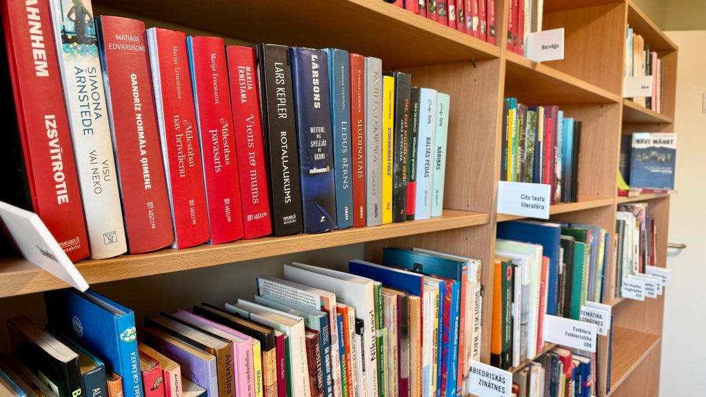 Tuvplāns jauniem grāmatu plauktiem ar dažādām, galvenokārt sarkanā krāsā iesietām, grāmatām bibliotēkā