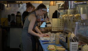 “Big Bad Bagels” darbiniece gatavo pasūtījumu kafejnīcas virtuvē.