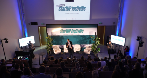 Plašs skats uz konferenču zāli Daugavpilī, kur uz skatuves notiek "StartUp" festivāla prezentācija