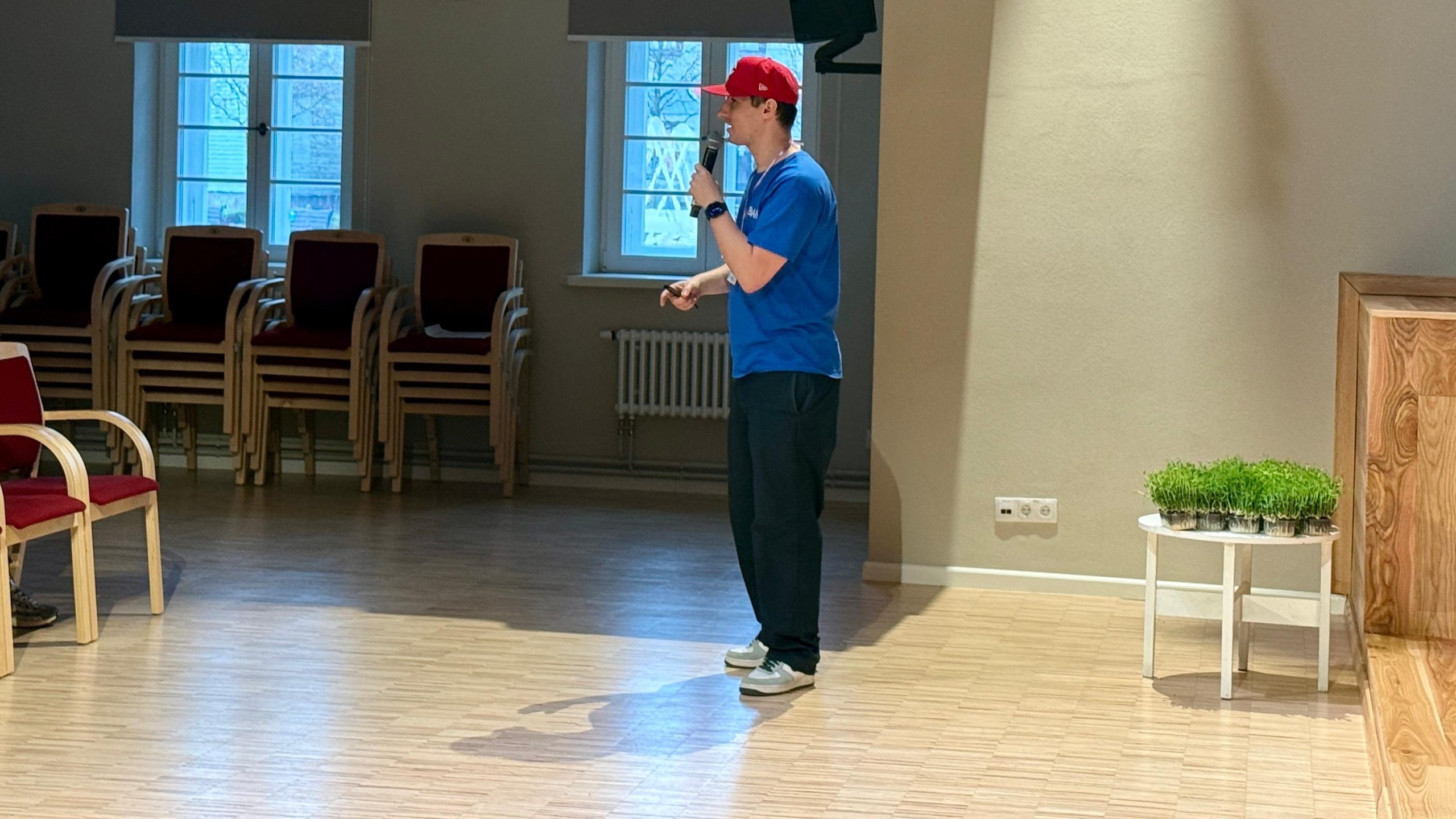Elviss Strazdiņš ar mikrofonu vada nodarbību vai lekciju zālē pie skatuves.