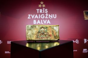Zelta stienim līdzīga balva ar trim zvaigznēm centrā, kas novietota uz melna postamenta, fonā redzams uzraksts "TRĪS ZVAIGŽŅU BALVA".
