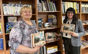Biedrības "Sērenes ļaudis" valdes priekšsēdētāja Edīte Osāne (pa kreisi) un bibliotēkas vadītāja Rea Vovere (pa labi) stāv pie grāmatu plaukta un demonstrē tikko izdoto Sērenes pagasta dzimtu stāstu krājumu.