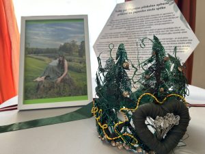 Pašdarināta meža tematikas galvas rota ar sirds dekoru izstādē pie fotogrāfijas un apraksta.
