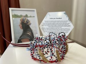 Roku darināta vainaga kompozīcija ar graudiem un pērlītēm pie teikas apraksta un fotogrāfijas.