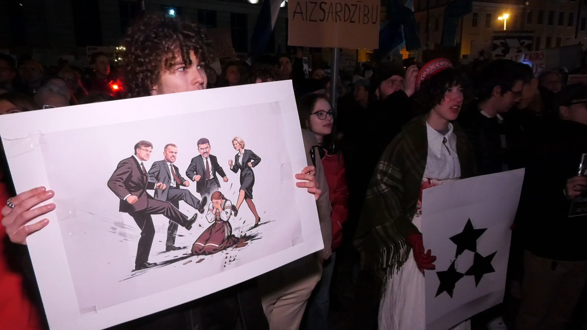 Protesta dalībnieki Doma laukumā Rīgā tur plakātu ar politisko karikatūru, kurā vara simboliski uzbrūk sievietei latviešu tautastērpā.