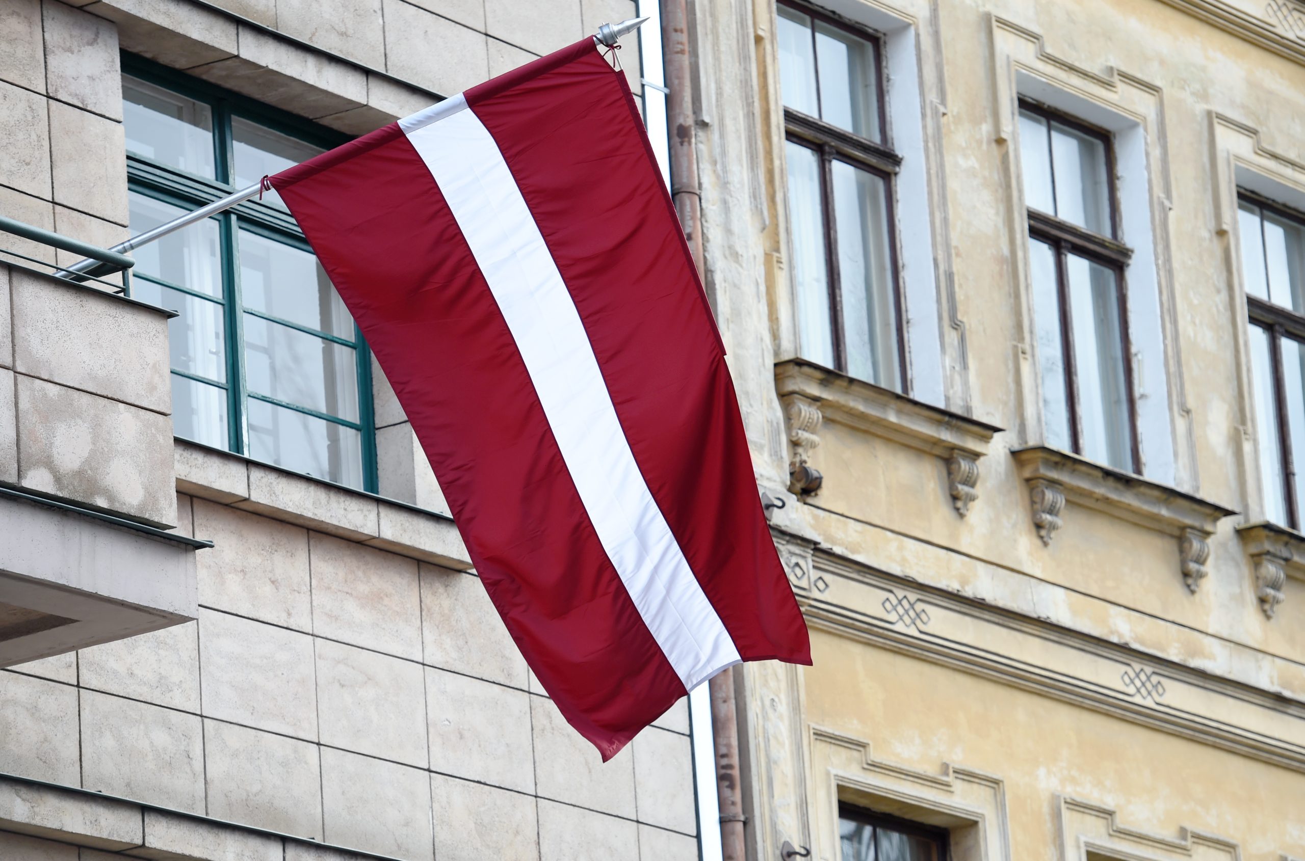 Latvijas valsts karogs pie ēkas fasādes svētku laikā.