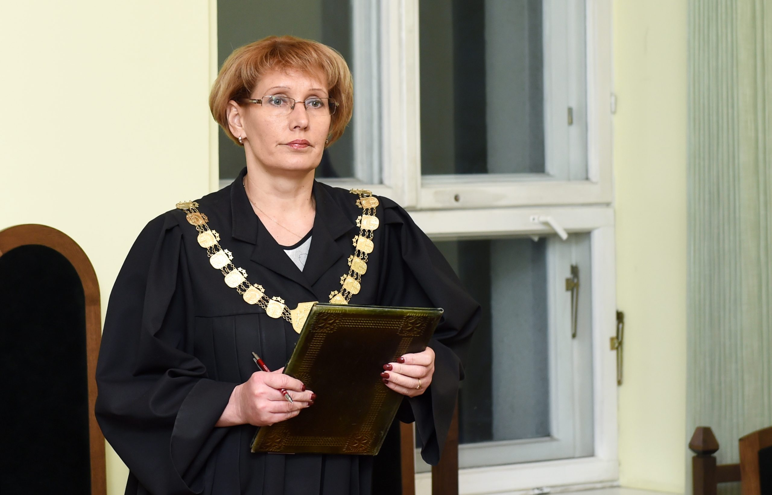 Tiesnese tiesas zālē, tērpusies mantijā un šķēdē ar dokumentu mapēm rokās.