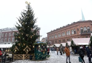 Rīgas Doma laukuma Ziemassvētku tirdziņš ar svētku eglīti, tirgotāju namiņiem un sniegputeni.