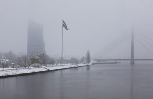 Rīgas panorāma ziemā ar Latvijas karogu un Vanšu tiltu miglā
