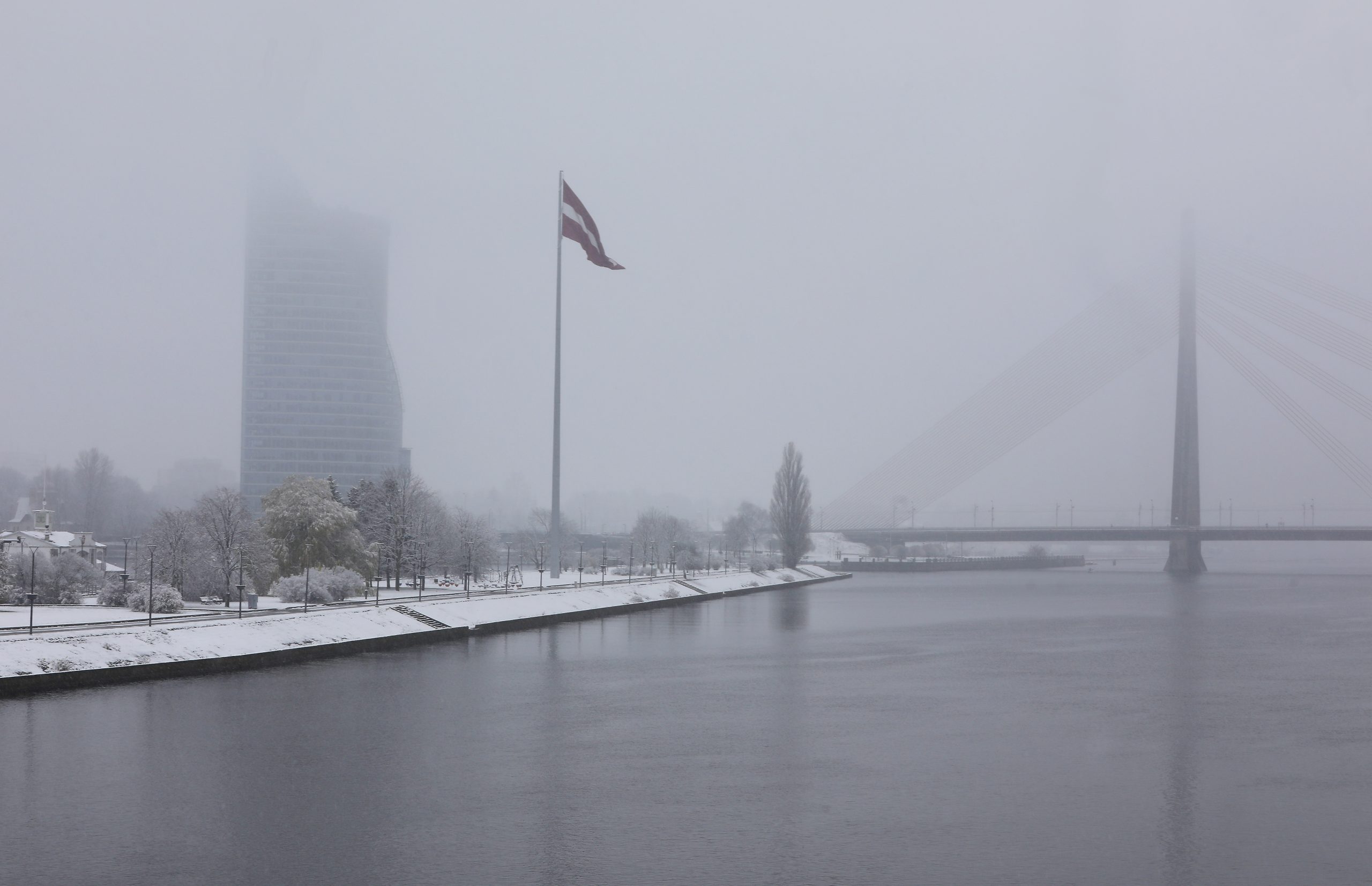 Rīgas panorāma ziemā ar Latvijas karogu un Vanšu tiltu miglā