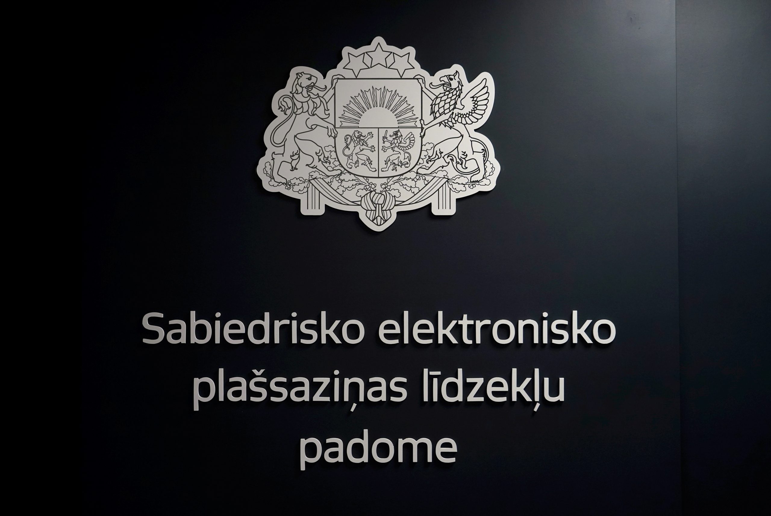 Latvijas valsts ģerbonis un Sabiedrisko elektronisko plašsaziņas līdzekļu padomes nosaukums uz sienas.