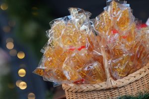 Dabisks pīts grozs, pilns ar caurspīdīgiem, dzelteni-oranžiem karamelizēta cukura saldumiem (gailīšiem) individuālos iepakojumos.