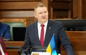 Edvards Smiltēns uzrunā klātesošos pie Saeimas tribīnes, viņa priekšā redzamas Latvijas un Ukrainas karodziņu miniatūras.