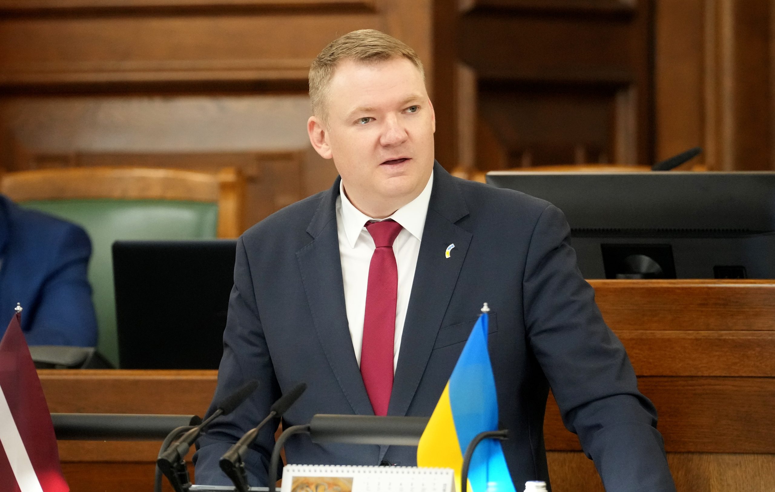 Edvards Smiltēns uzrunā klātesošos pie Saeimas tribīnes, viņa priekšā redzamas Latvijas un Ukrainas karodziņu miniatūras.