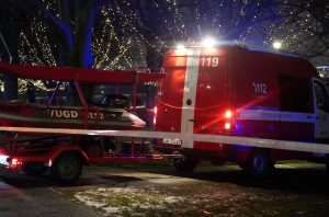 Valsts ugunsdzēsības un glābšanas dienesta (VUGD) sarkanais furgons un piekabe ar glābšanas laivu tumšā naktī pie ūdens.