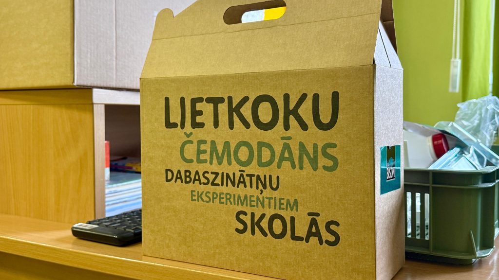 Brūna kartona kaste ar lielu uzrakstu: "LIETKOKU ČEMODĀNS DABASZINĀTŅU EKSPERIMENTIEM SKOLĀS"
