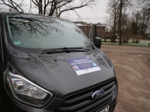 Transports pēc pieprasījuma mikroautobuss ar informatīvu uzlīmi uz motora pārsega.
