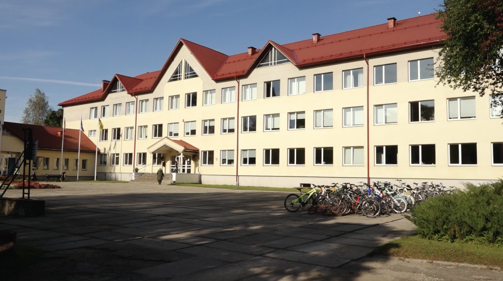Skolas ēka ar sarkanu jumtu un velosipēdiem pie ieejas