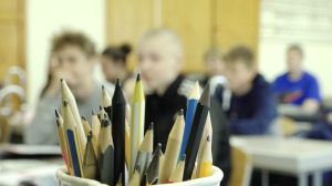 Zīmuļu trauks klasē ar skolēniem fonā