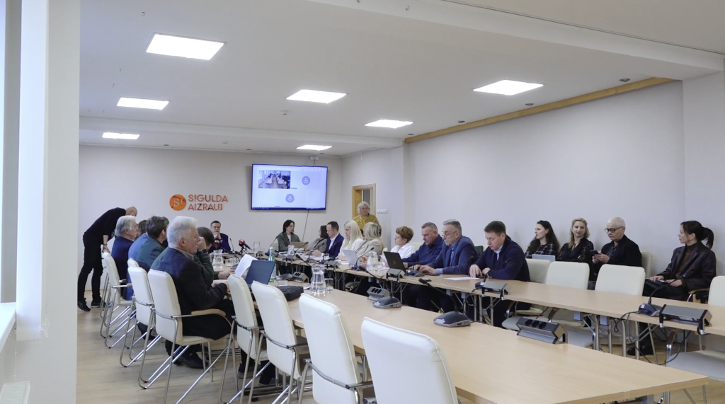 Siguldas novada domes sēžu zāle ar deputātiem pie gara galda.