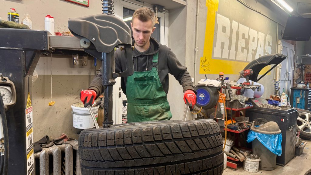 Autoservisa darbinieks strādā ar riepu montāžas iekārtu.