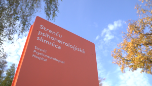 Strenču psihoneiroloģiskās slimnīcas informatīvā zīme pie ieejas ēkā saulainā dienā.