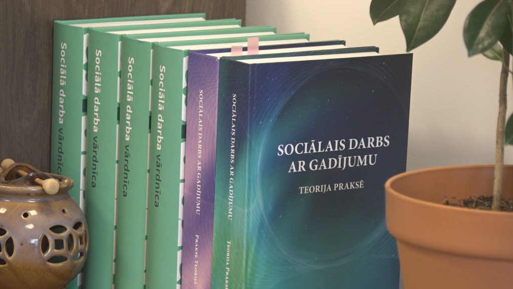 Tuvplāns uz grāmatu plaukta ar grāmatām "Sociālā darba vārdnīca" un "Sociālais darbs ar gadījumu: Teorija un prakse".