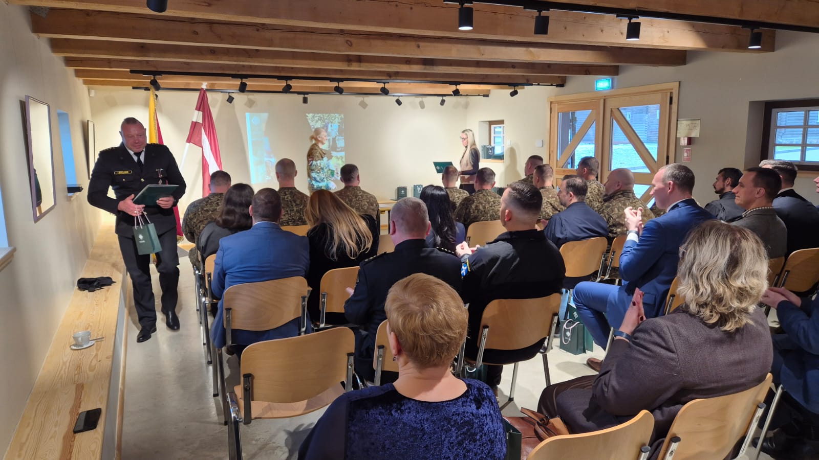 Svinīgā pasākumā zālē sēž militārpersonas un viesi, bet priekšā uzstājas runātāja.